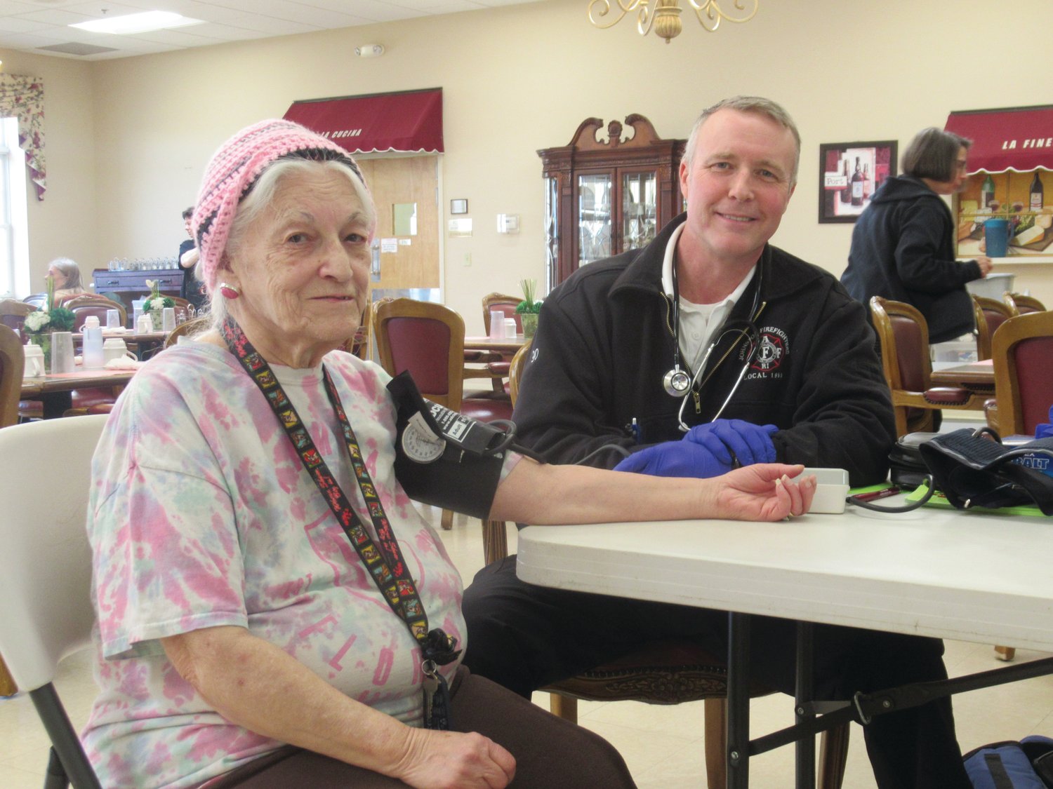 SMILING SERVICE: JFD Battalion Chief Tom McCormick adjusts a blood pressure monitor to the arm of Gloria Renzi during last Thursday’s unique and first-ever Blood Pressure Screening Event at the Johnston Senior Center.